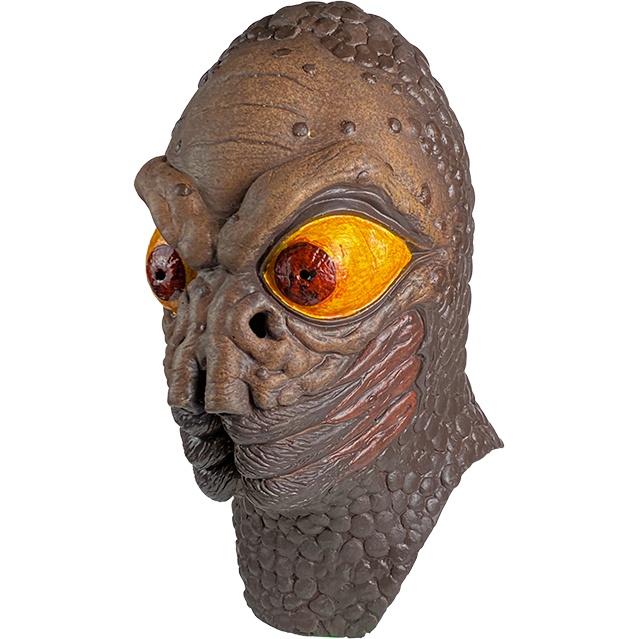 Mask, head and neck, left view. Brown, wrinkled and bumpy skin. Heavy brows large red and yellow eyes, two large nostrils under eyes, insect-like mouth.