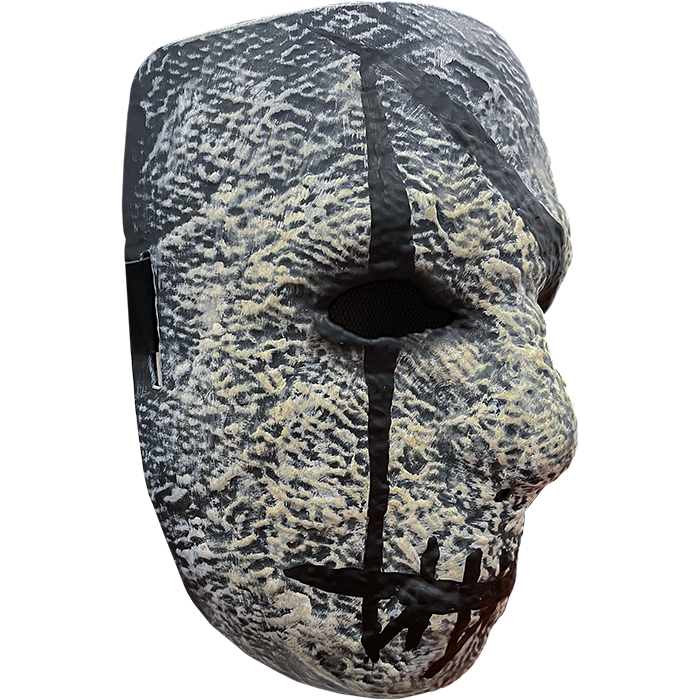Plastic face mask. Gray stone textured, nondescript facial features, black painted i over right eye, mouth is horizontal black line with several vertical hash marks.