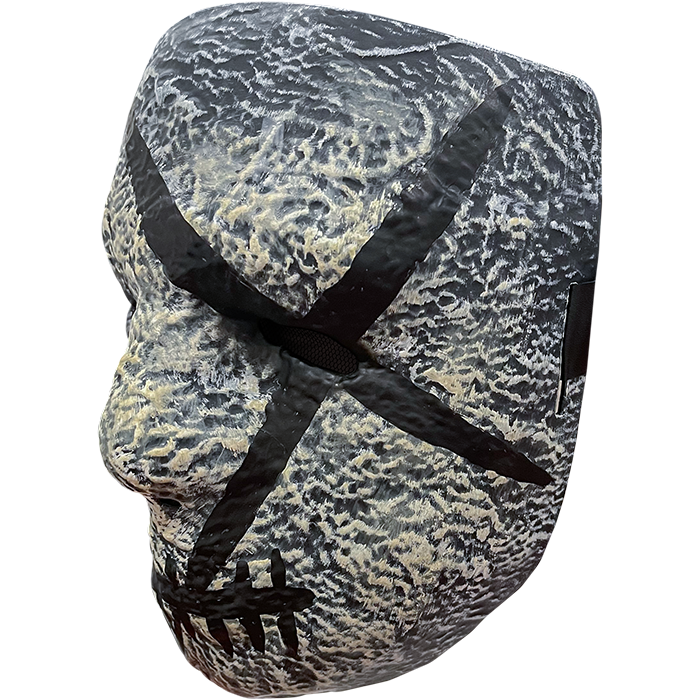 Plastic face mask. Left side view Gray stone textured, nondescript facial features, black painted x over left eye, mouth is horizontal black line with several vertical hash marks.