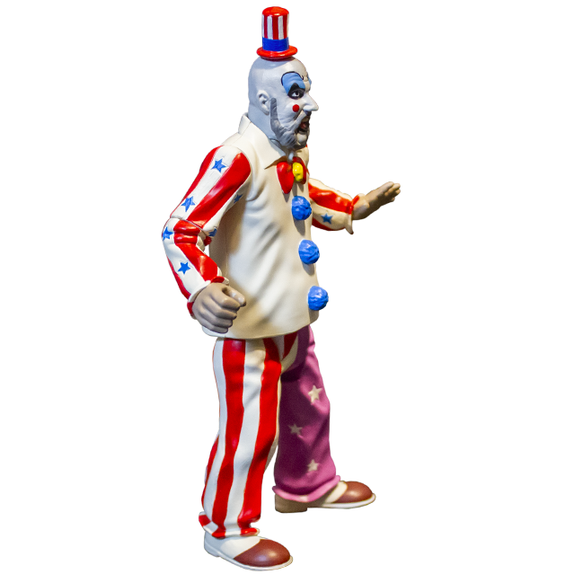 Captain Spaulding action figure, right side view. Bald man, red and white striped small top hat with blue band, white clown makeup, high black eyebrows, blue eyeshadow, black circles around eyes, pink spots on cheeks, large menacing grin, full gray beard, wearing white collared shirt, red and white striped sleeves with blue stars, red bow at collar, skull pin, blue pompoms, pants right leg red and white striped, left leg purple with white stars, brown and white shoes.