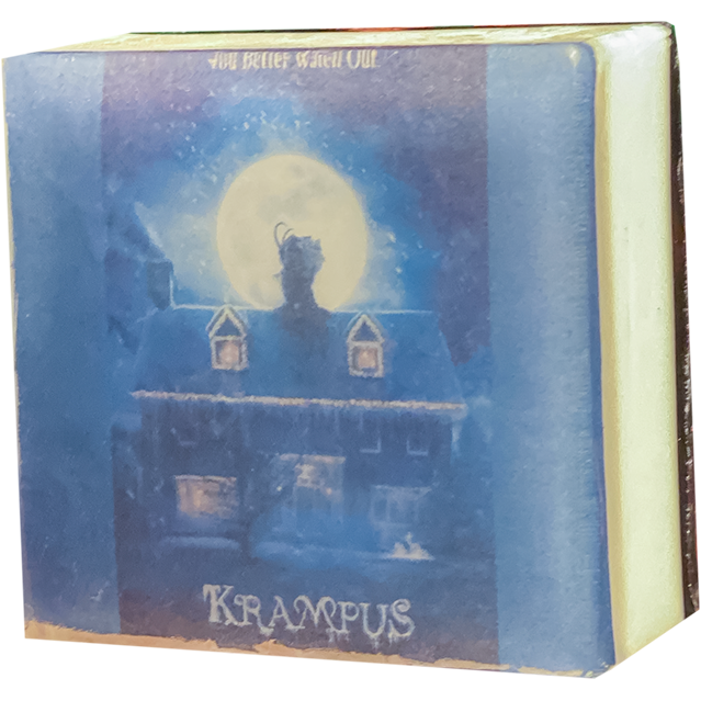 Bar soap. White, with illustration of a nighttime movie scene, full moon, silhouette of Krampus on the rooftop of a house, white text reads Krampus, under clear soap layer. 