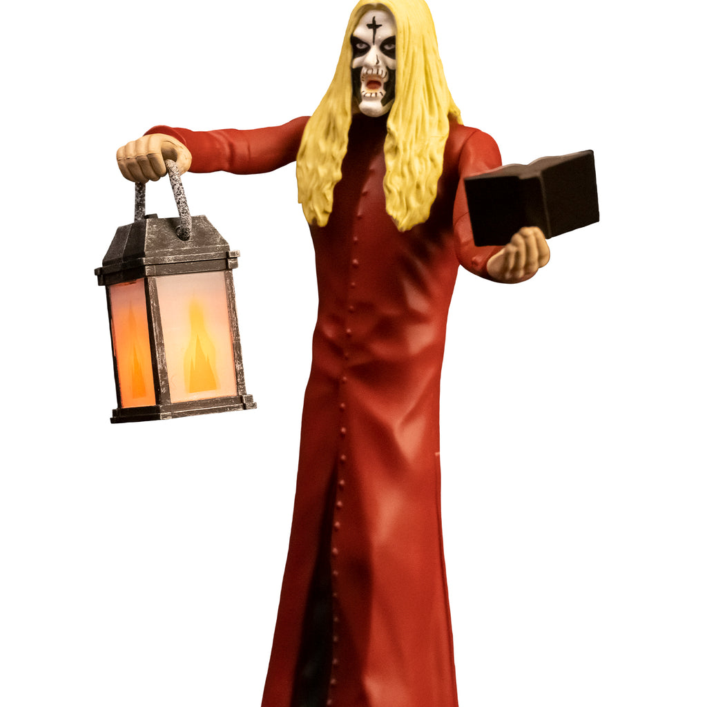 Action figure, close up view. Man, blond hair, white face with black cross on forehead, black around eyes, mouth and cheeks. Wearing floor length red, button down coat, holding book in left hand, lantern in right hand.
