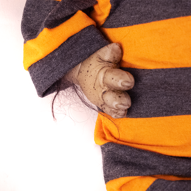 Close up view of paw like right hand with claws, sparse black fur on arm. Wearing gray and orange striped pajamas.