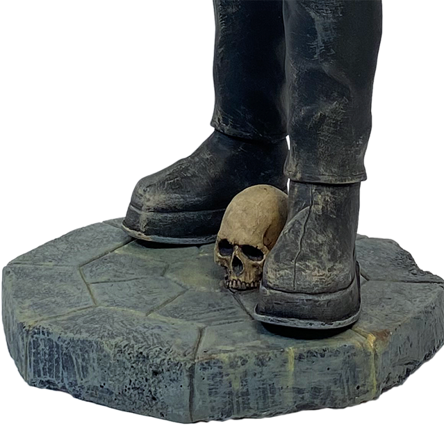 Frankenstein statue, close up of base. Dirty black pants, large black shoes, set on gray, stone textured base, skull between feet.