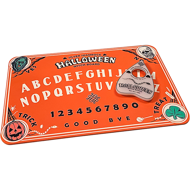 Orange Witch board.  Top left corner green witch face, text reads Yes.  Top right corner skull face, text reads no.  Bottom left Jack o' lantern, text reads Trick.  Bottom right corner, green shamrock, text reads Treat.   Center of board, top to bottom text reads Silver Shamrock Halloween Witch Board.  entire alphabet a through m and then N through Z, numbers 1 through 0 text at bottom reads Good Bye.  White planchette sitting on board.