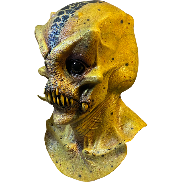 Mask, head neck and upper chest, left side view. Bald Alien head, black spots in center of crown of head. Large, pronounced brows and cheekbones. Large, shiny black eyes. No nose. Mouth with several sharp yellow teeth and two large tusks.