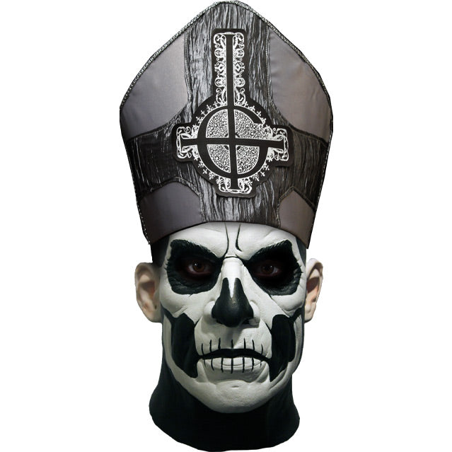 Mask, front view. Head and neck. Bald, black painted head and neck, white painted face, with black accents to create skull like appearance. Wearing black and silver, tall hat adorned with inverted cross, with semi circle that looks like a G.