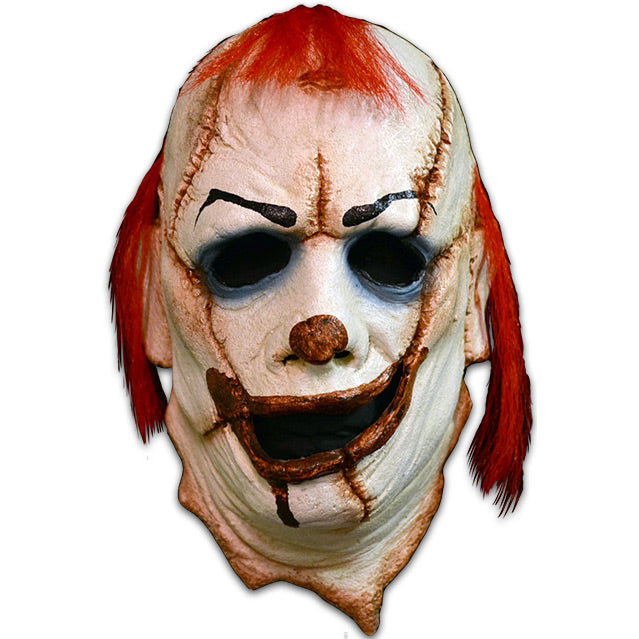Clown mask, pieces stitched together.  white skin, red nose, grotesque wide red mouth, blue rings around eyes.  sparse shaggy red hair on forehead and over ears.