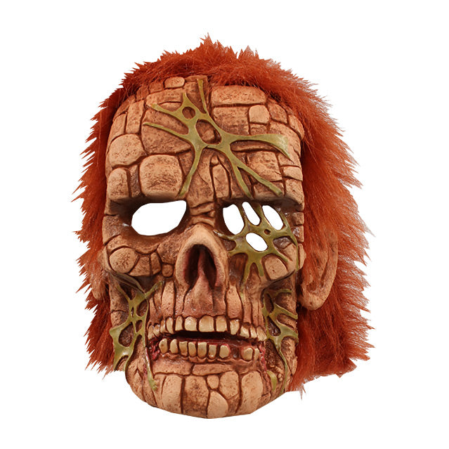 Front view of Mask. Skull-like face, made up of squares made to look like stones, Sinew- like webbing across forehead, left eye socket and both sides of jaw, short bushy red hair.
