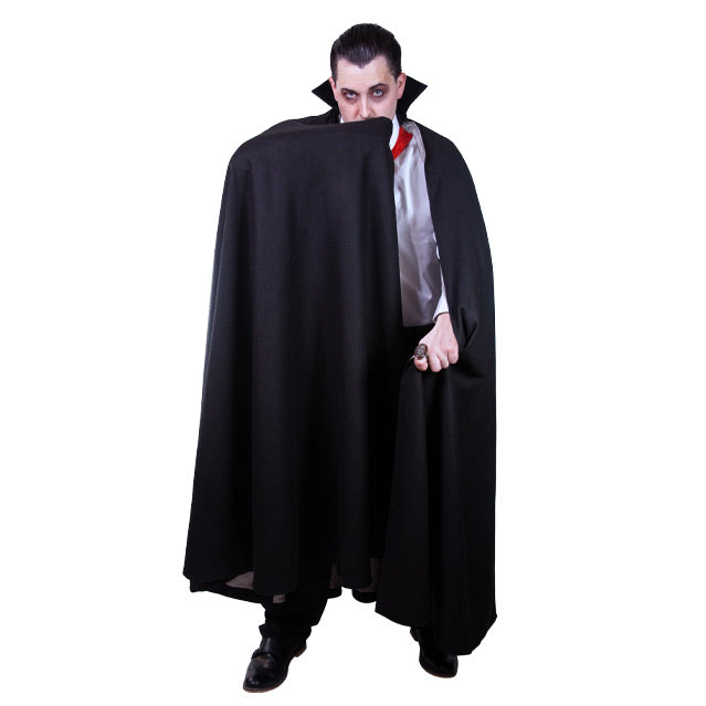 Man dressed as a vampire, front view.  Black hair, white shirt with red around the collar.  Black cape with standing collar. man is holding the cape in front of his mouth with his arm,