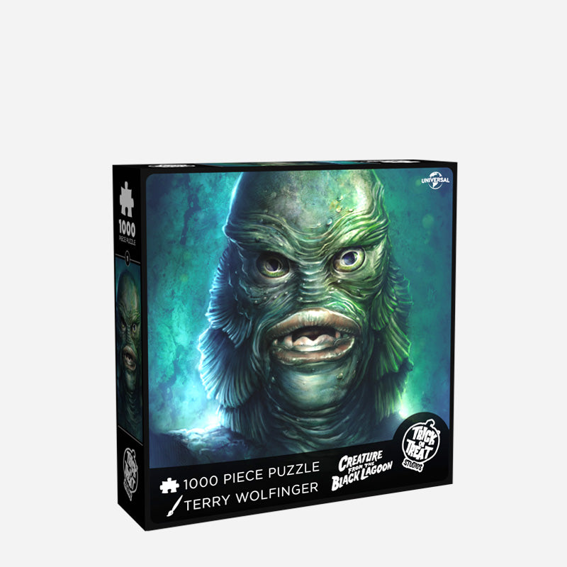 Product packaging. Cover. Black box, white text reads 1000 piece puzzle, Terry Wolfinger, creature from the Black Lagoon, white Trick or Treat Studios logo. Illustration of the Creature from the Black Lagoon, blue background, fish man face covered in green scales, large-lipped fish mouth.