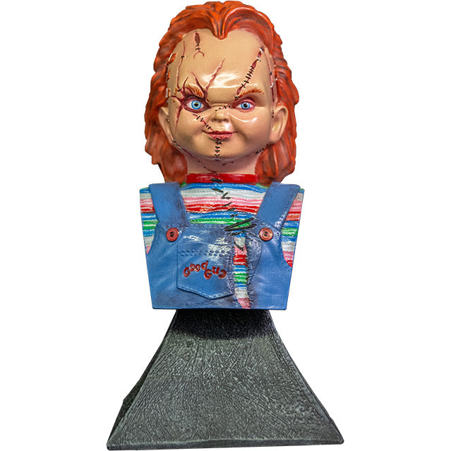 Front view.  Scarred Chucky mini bust, red hair, blue eyes, scarred face.  Wearing a red, white, blue and green striped shirt, ripped blue overalls with red buttons, red Good Guys printed on pocket.  Head, neck, and chest attached to gray stone textured base.