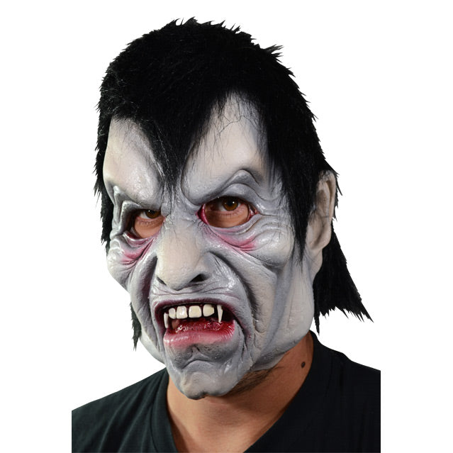 Left side view. Man wearing vampire mask. Pale gray skin, Black hair with deep widow's peak, creased skin around forehead, eyes and mouth.