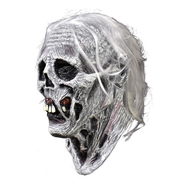 Left side view. Chiller mask. White and grey skeletal face with wrinkled and rotten flesh, black eye sockets, prominent teeth in dark red gums. bright white hair.