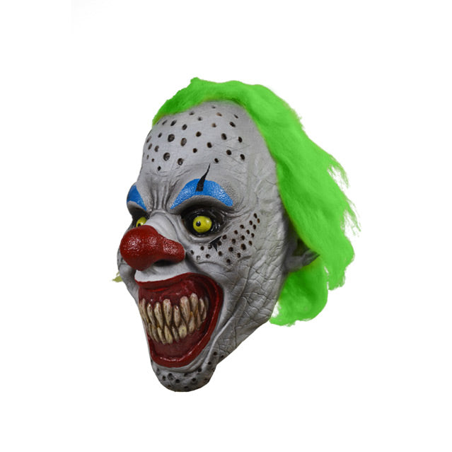 left side view. Scary Clown face. Bright green hair, white skin with black holes, black ringed yellow eyes with blue eyebrows, large bright red nose, large red clown mouth smiling with large sharp teeth.