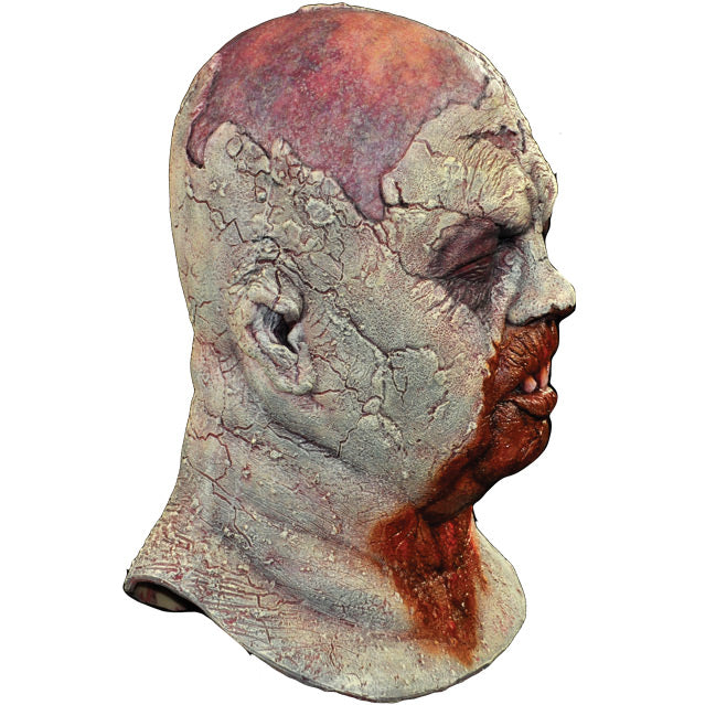 Mask right side view. Zombie, head and neck. Bald head, rotten skin, eyes closed, gory mouth missing teeth, blood from mouth running down chest.