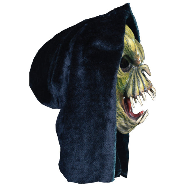Right side view. Light and dark green faced creature in black hood, wrinkled skin, wide open mouth showing tongue and several large fangs.