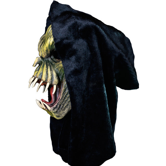 Left side view. Light and dark green faced creature in black hood, wrinkled skin, wide open mouth showing tongue and several large fangs.