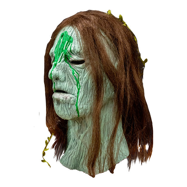 Left side view, Creepshow Becky Mask, Zagone edition. Head and neck of woman. Red brown straight hair, with seaweed in it, green wrinkled mossy skin, eyes appear closed. hole in forehead oozing dried green fluid.