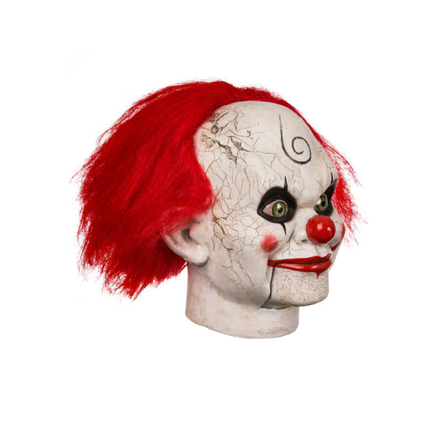 Right side view. Mary Shaw Clown Mask, head and neck. Distressed finish white skin, ventriloquist dummy clown face, spiral curl drawn on forehead, rosy red spots on cheeks, red nose, bright red hair, black-rimmed, bloodshot green eyes. Bright red grinning lips, hinged lower jaw.