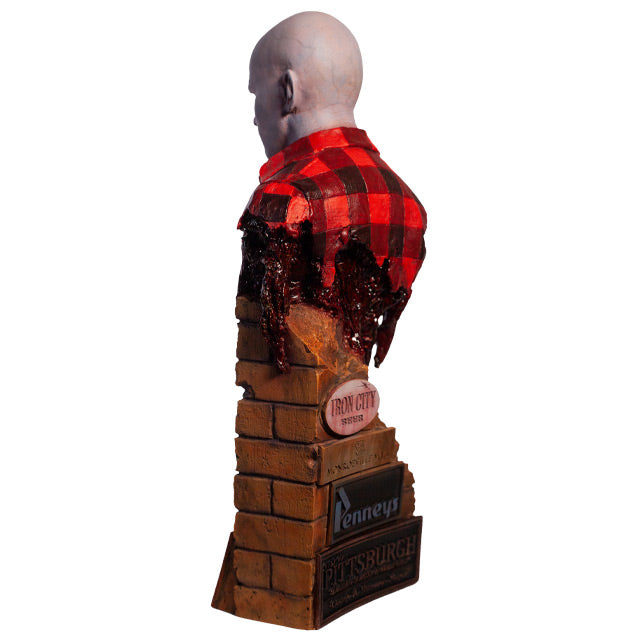 Left side back view. Airport Zombie bust. Head shoulders and upper torso. Bald zombie, right side of face and chest is gory, wearing torn red and black flannel shirt, with gore hanging from left shoulder and back. Base of bust is a broken brick wall, signs at bottom in back.