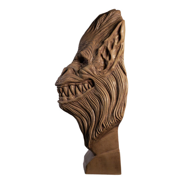 Left side view. Crate Beast bust. Clay colored, beast face, wrinkled skin, eyes with vertical long pupils, pointed ears, snout nose, large grinning mouth with many sharp teeth, long hair covering head, lower face and neck. Set on a base.