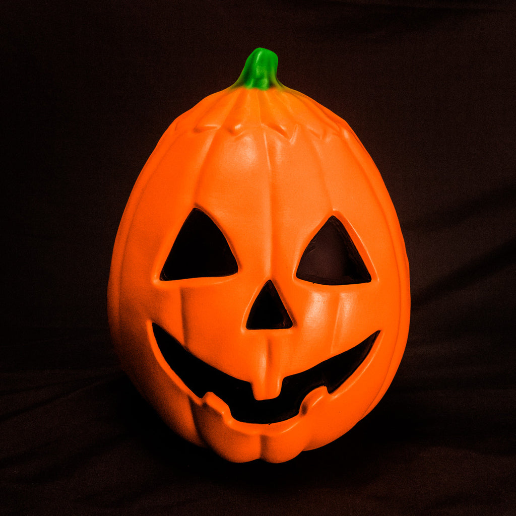 Un-lit Pumpkin prop, front view. Orange jack o' lantern, green stem, black triangle eyes and nose, grinning black mouth.  On black background.