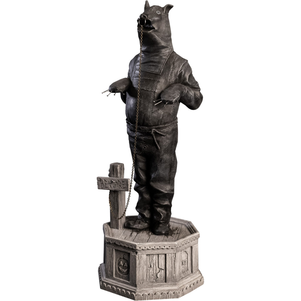 Left side view, statue. Grayscale, Person in leather bondage bear costume, with metal claws on hands, ring in nose attached to chain that is attached to a cross, that says Beware, by his feet. Standing on hexagon base made of gravestones.