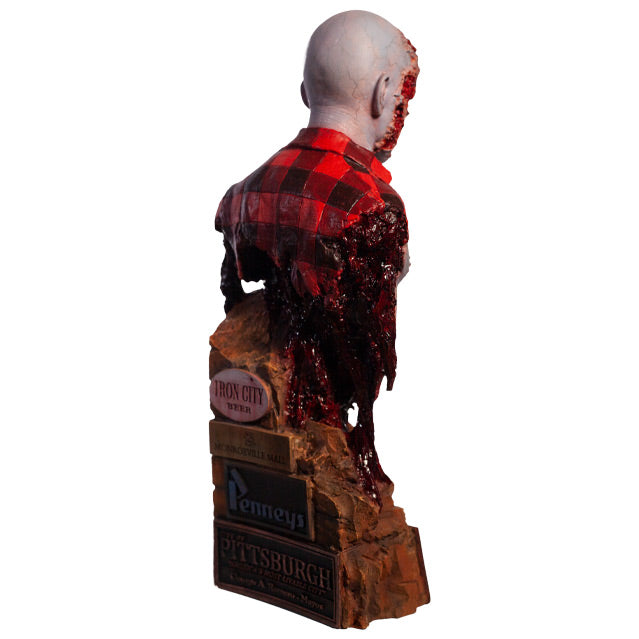 Right side back view. Airport Zombie bust. Head shoulders and upper torso. Bald zombie, right side of face and chest is gory, wearing torn red and black flannel shirt, with gore hanging from shoulder and back. Base of bust is a broken brick wall, signs at bottom in back.