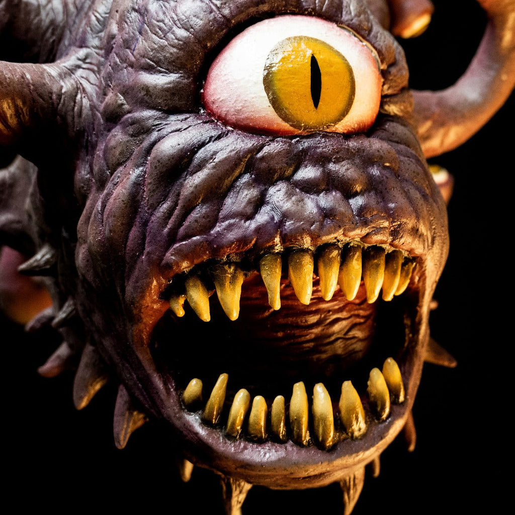 Mask face close up view on black background with dramatic lighting. Purple gray lumpy flesh. 10 protruding eye stalks with yellow eyes. one large yellow eye with a vertical pupil, in the in center of head. Spikes around jawline and on neck, gaping open mouth with large sharp teeth.