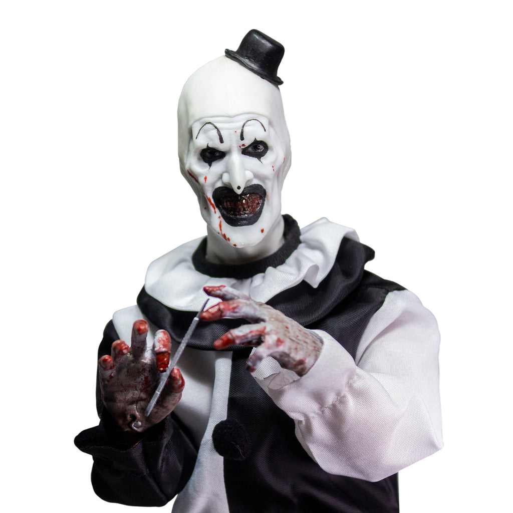Terrifier, 1/6 scale figure, close up view. Evil grinning clown face with tiny black top hat, black and white, jumpsuit, ruffle at neck, fingerless white gloves. Blood spatter on face and hands. Holding scalpel in right hand.