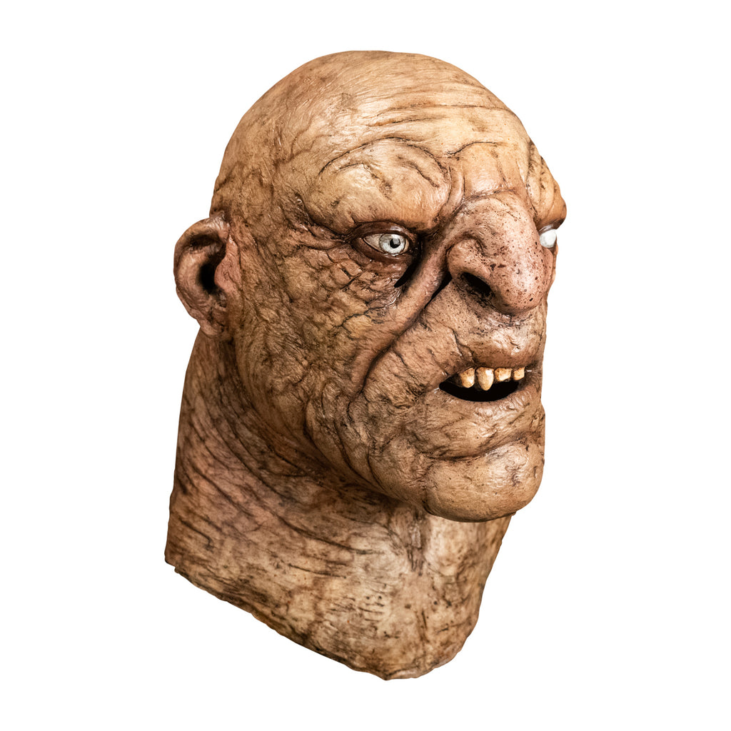 Mask, head and neck, right side view. Troll, bald, wrinkled and dirty tan skin, large nose and chin, mouth open showing teeth. Small ears, right eye blue, left eye white. Thick neck.