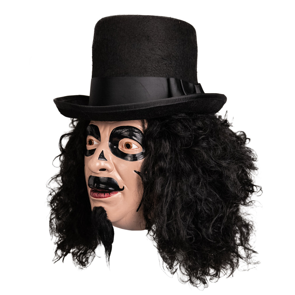 Mask, left side view. Man, long, black, curly hair, black top hat, long black goatee, brown eyes. Black face paint, circles around eyes, small triangles on either side of bridge of nose, curved lines on cheeks, large painted on moustache.