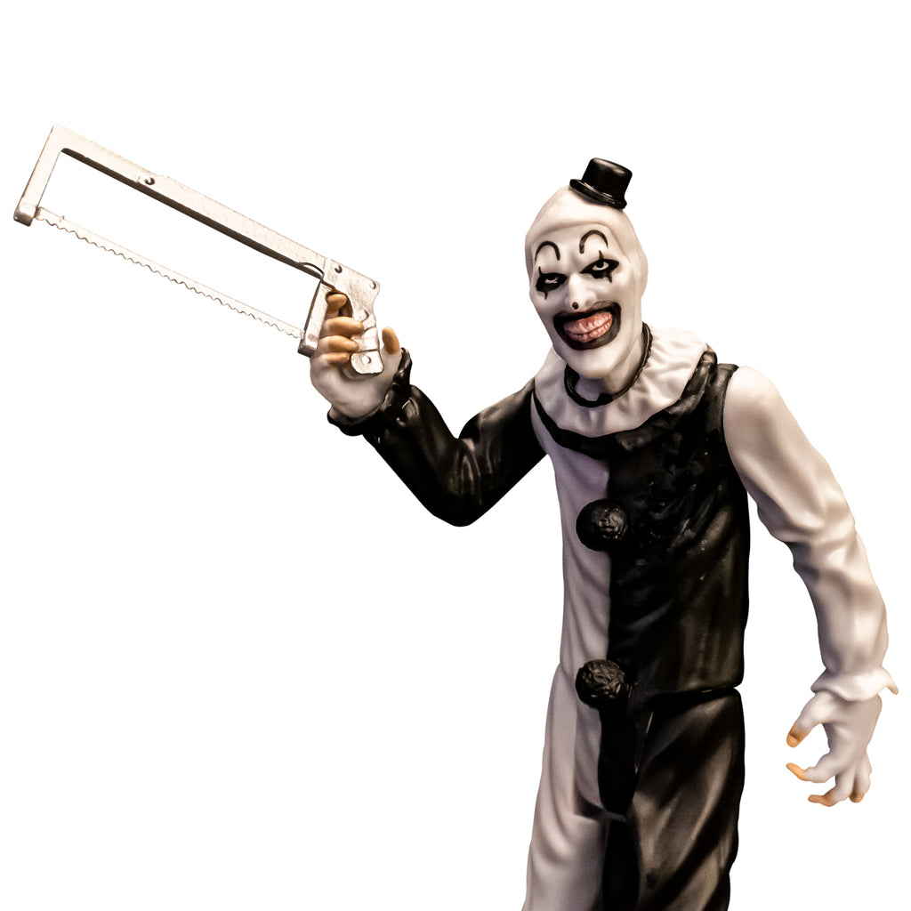 Terrifier, 5 inch figure, close up. Evil grinning clown face with tiny black top hat, black and white, jumpsuit, ruffle at neck, fingerless white gloves holding saw in right hand. 