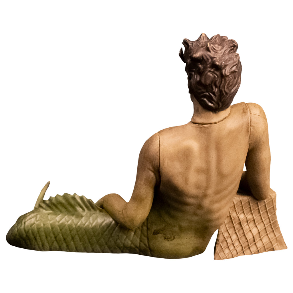 Action figure. Back view. Fishboy, merman with short brown hair, green fish tail, resting right arm on brown stone.