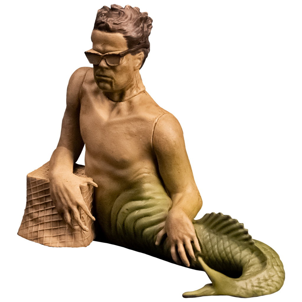 Action figure. Fishboy, merman with short brown hair, glasses, green fish tail, resting right arm on brown stone.