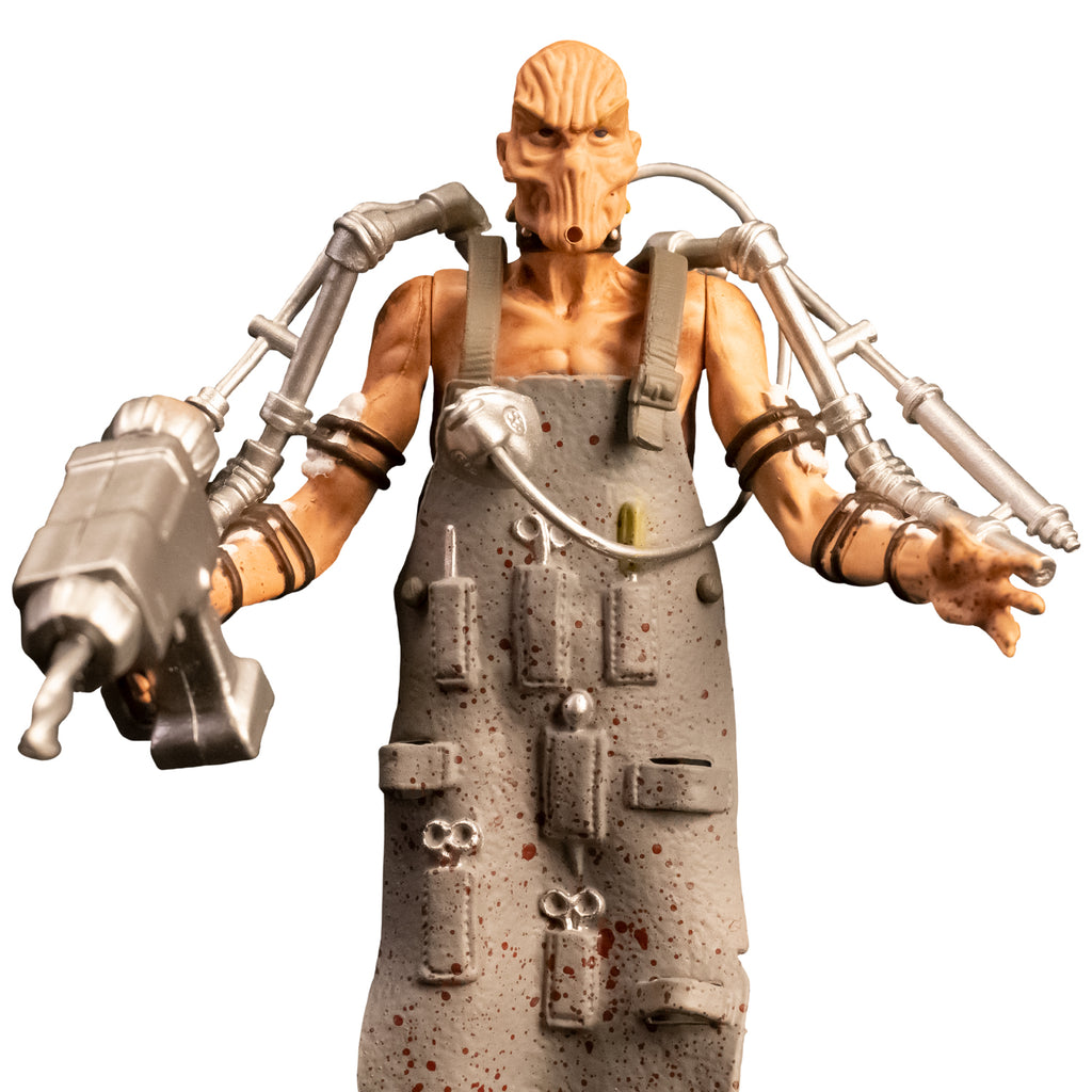 Action figure, close up front view. Bald man with wrinkled skin, missing mouth, black collar, gray apron with pockets holding medical instruments, shirtless.  Silver drill tools attached to both arms with black straps.