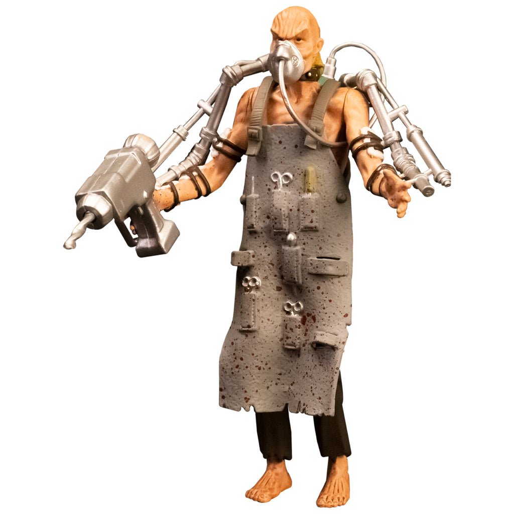 Action figure, left front view. Bald man with wrinkled skin, wearing oxygen mask, black collar, gray apron with pockets holding medical instruments, shirtless, brown tattered pants, bare feet. Silver drill tools attached to both arms with black straps.