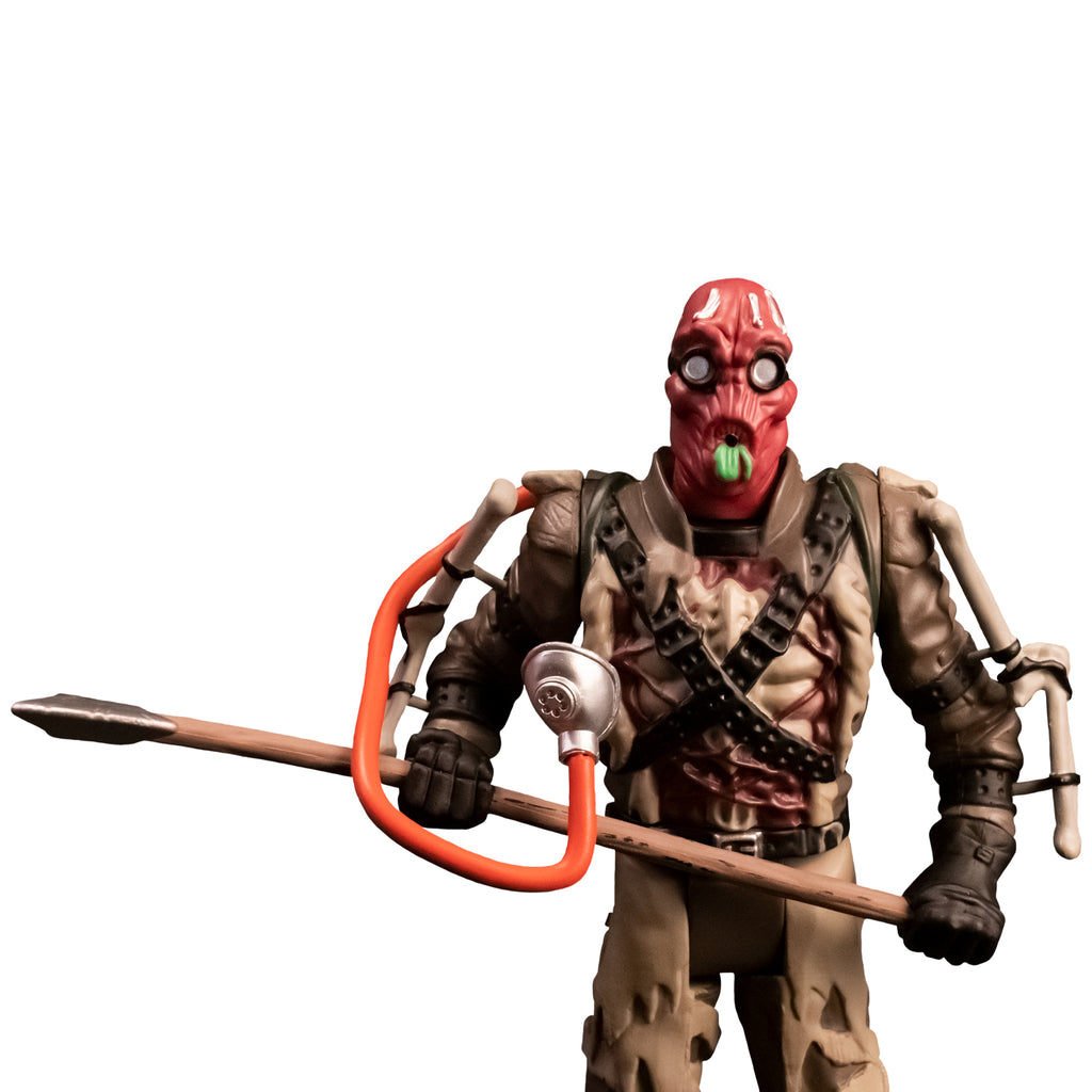 Action figure. Close up front view. Person with red head, wearing goggles puckered mouth with green tongue. Oxygen mask with orange hose. Tattered brown and tan outfit, apparatus attached to arms, ammunition belts across chest, black gloves. Holding large Axe.