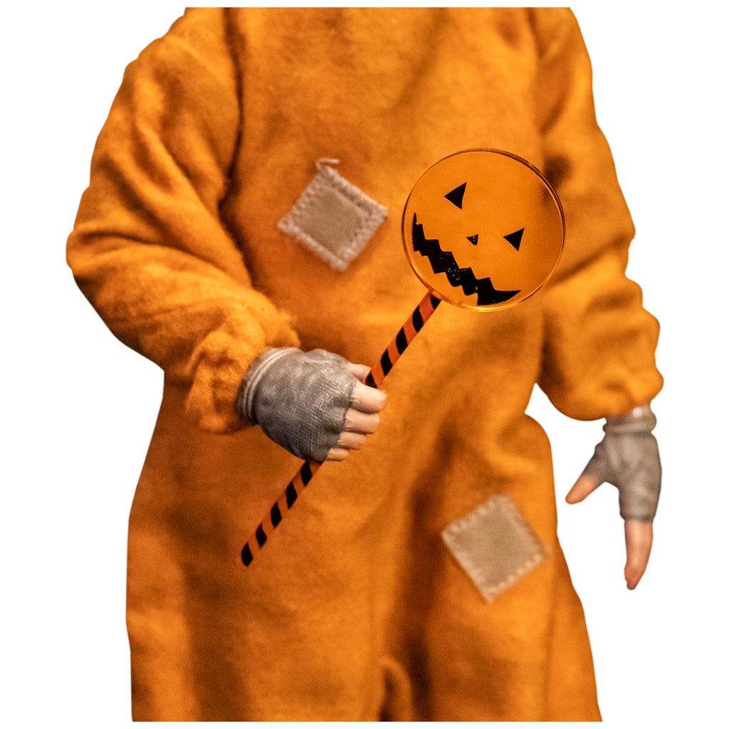Close up view of  jack o' lantern lollipop held by Sam in orange pajamas, brown fingerless gloves.