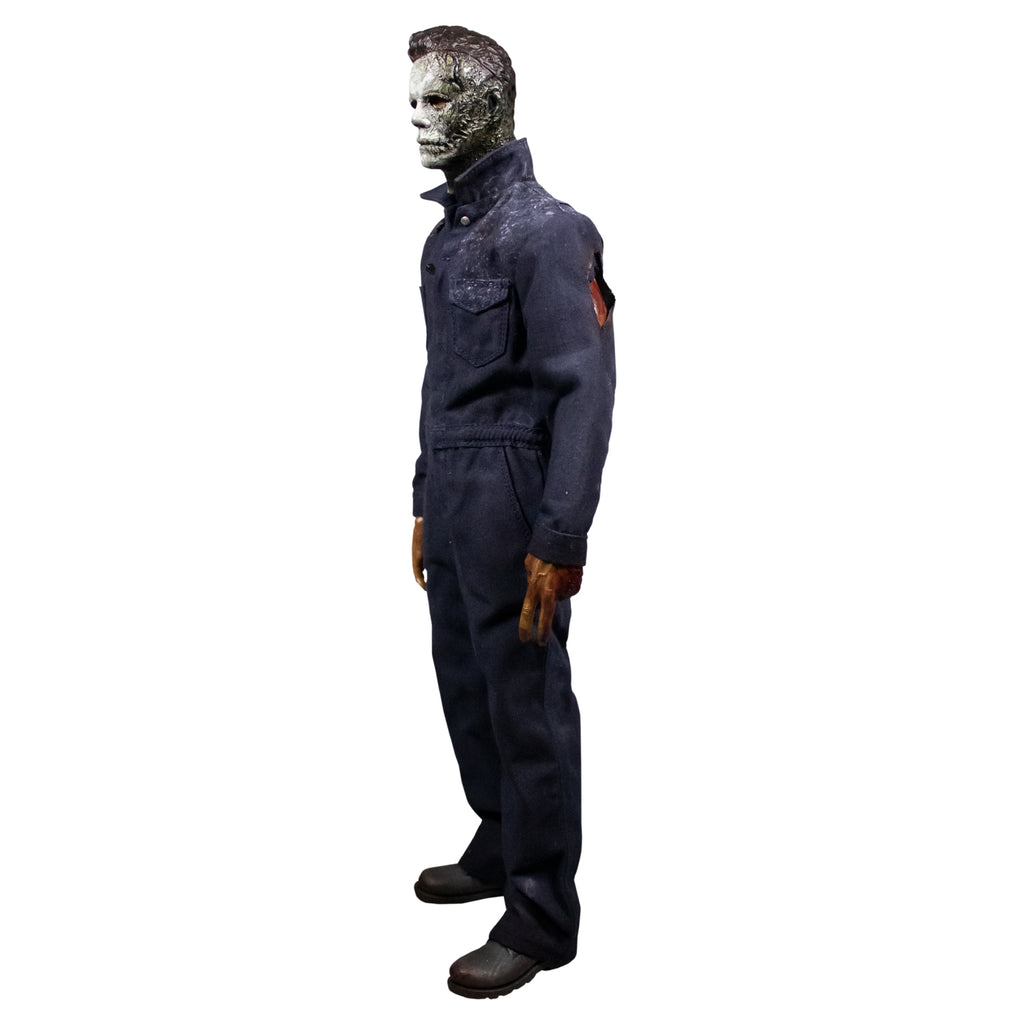 Left side view, Michael Myers 12 inch action figure. Wearing Halloween kills mask damaged left side of face, blue coveralls with slice on upper left arm, left hand missing 2 fingers, black boots.