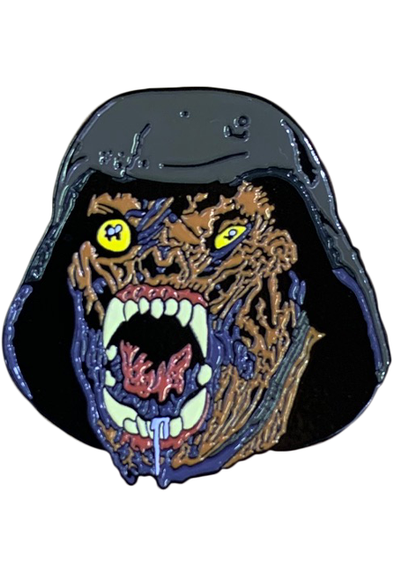 Enamel pin. The head of a creature wearing a World War 2 helmet. rotting flesh. Dark yellow eyes, right eye bulging. Shriveled nose. Open, drooling mouth with rotten tongue, large teeth and fangs.