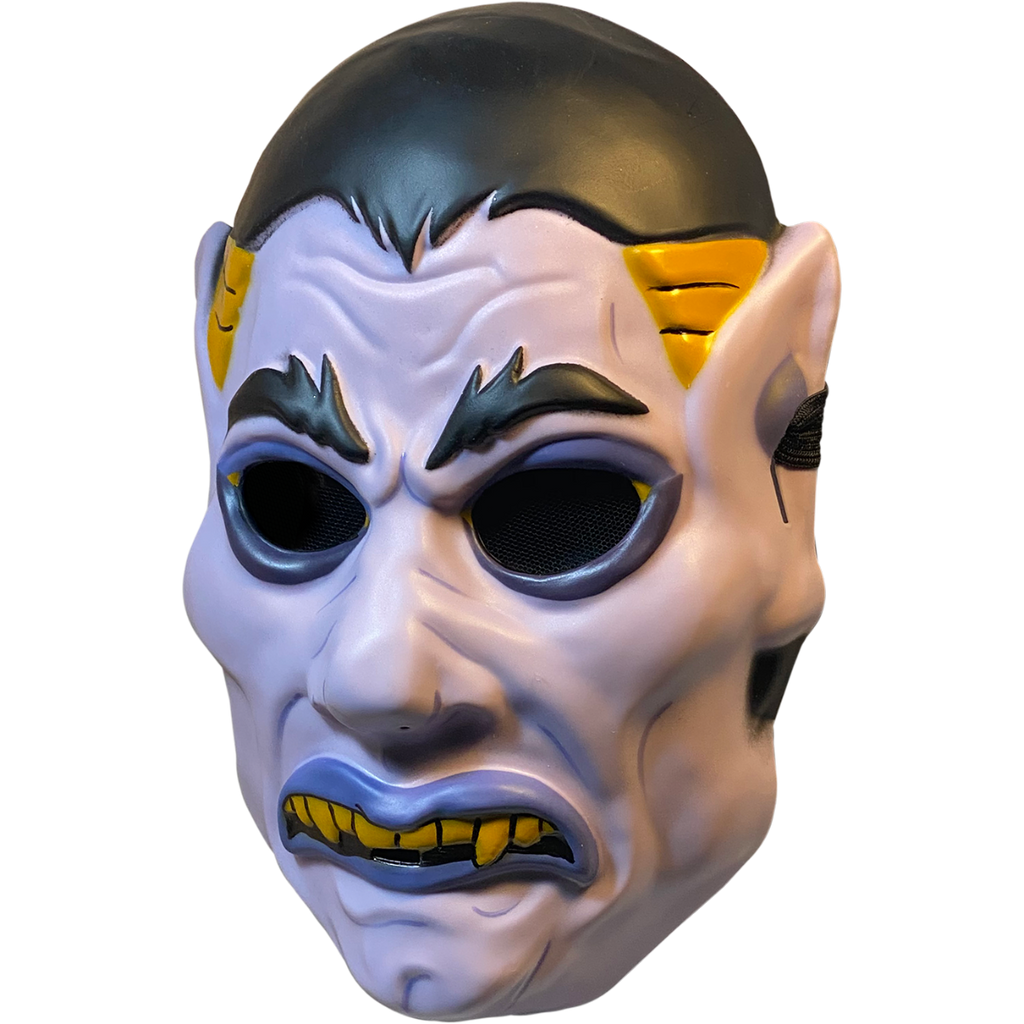 Plastic mask, left side view. White vampire face. Black hair, eyebrows and eyes. Blue-gray eyeliner and lips. Frowning mouth with yellow teeth and fangs. Yellow at temples. Pointed ears.