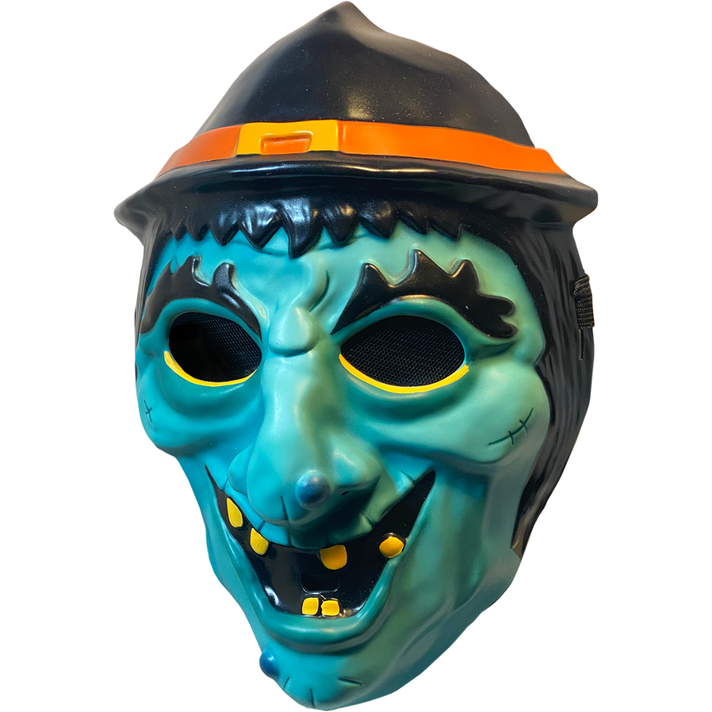 Plastic mask, left side view. Green witch face. Black hair, eyebrows and eyes. Black witch hat with orange band and yellow buckle. Yellow eyeliner under eyes. Grinning mouth with sparse yellow teeth.