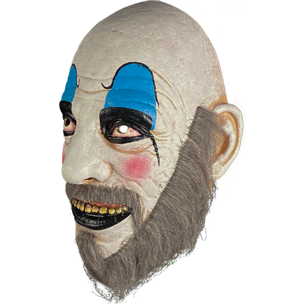 Mask, left side view. Bald man in white clown makeup, high black eyebrows, blue eyeshadow, black circles around eyes, pink spots on cheeks, large menacing grin, black bottom lip, full gray beard.