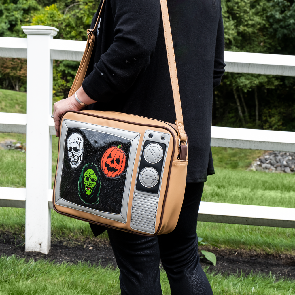 Person wearing bag, front view, made to look like a vintage TV with knobs. Static on the screen with skull, jack o' lantern and witch faces, tan with strap.