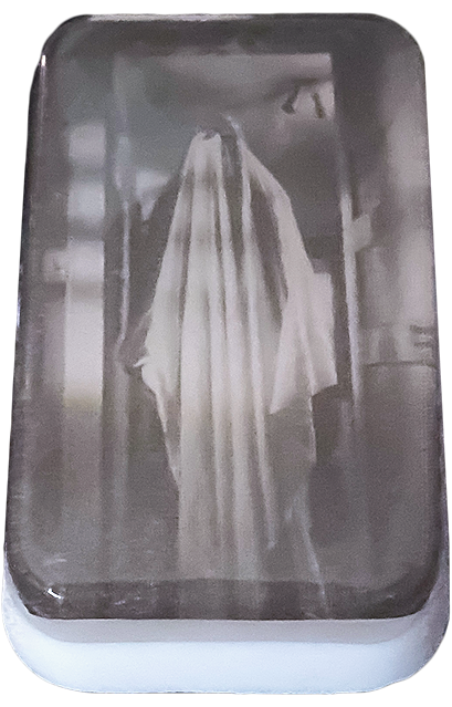 Bar soap. White, with black and white illustration of a sheet ghost standing in a doorway, under clear soap layer. 