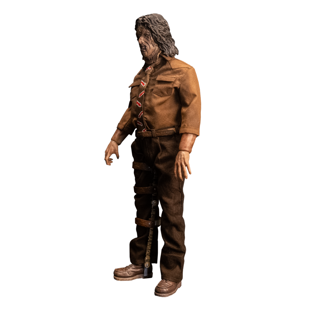 Action figure. Left view. Patchwork mask made of skin, brown hair. Wearing brown collared shirt and brown, red and white necktie, dark brown pants and belt. Brown shoes. Brown leg brace on right leg.
