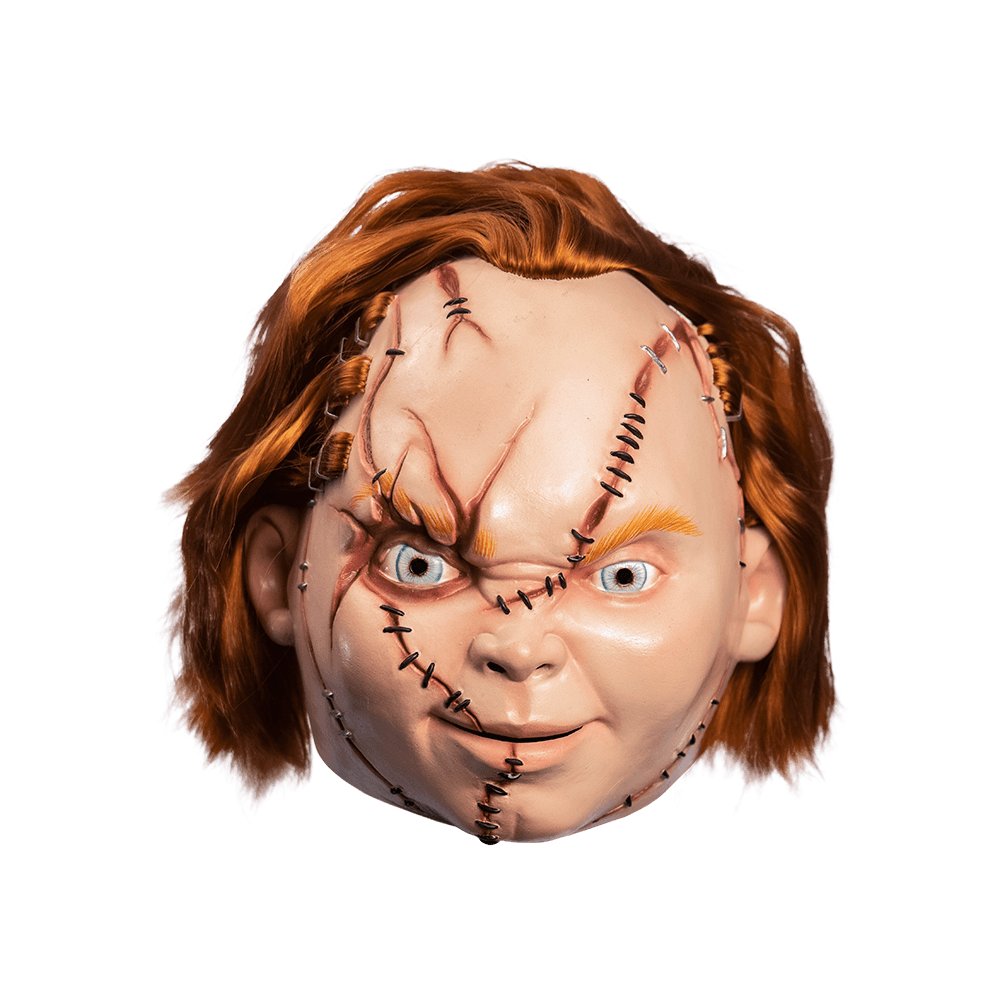 Front view. Scarred Chucky mask. Red hair, blue eyes, freckles, grinning mouth with teeth showing, cleft chin.  Face has many wounds, stitches and staples, sections of hair stapled on.