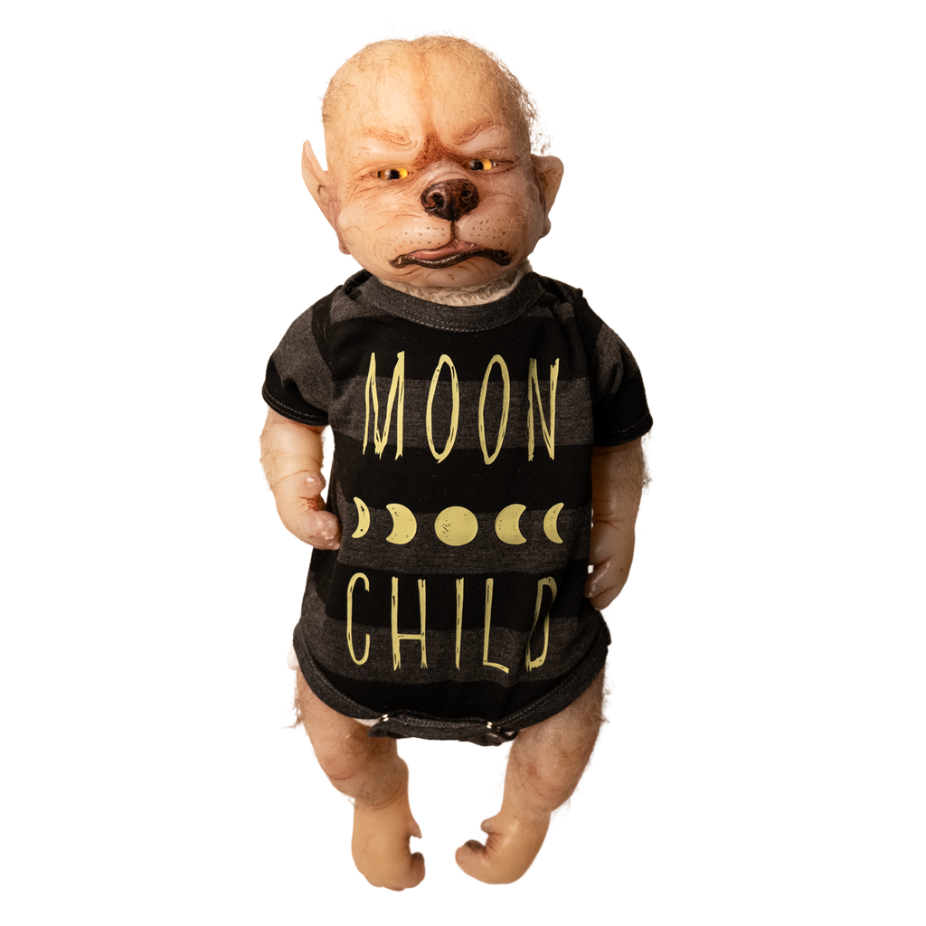 Doll. Full body view, standing. Tan skin, pointed ears on side of head, sparse light fur on head and arms. Gold eyes, canine nose, mouth with pink tongue slightly sticking out. Paw like hands and feet with claws. Wearing black and gray striped short-sleeved onesie, yellow moon phases, Yellow text on shirt reads Moon Child